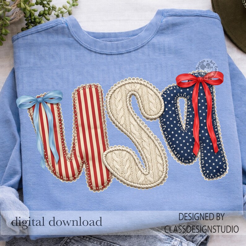 Puede incluir: Sudadera azul claro con las letras "USA" aplicadas. La "U" es a rayas rojas y blancas, la "S" es de punto de cable y la "A" es azul marino con estrellas blancas. Cada letra tiene un borde decorativo y un lazo.