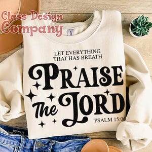 May include: A beige sweatshirt with the text "Let everything that has breath Praise the Lord" in black lettering. The text is in a retro font style with stars around it. The text "Psalm 15:06" is also included in black lettering.