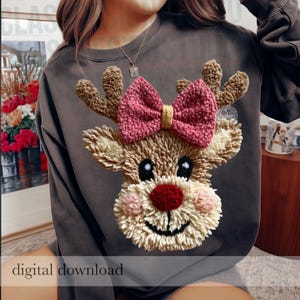 Könnte beinhalten: Ein dunkelgraues Sweatshirt mit Rundhalsausschnitt und einem texturierten Rentier-Motiv im Punch-Needle-Stil. Das Rentier hat beiges Fell, eine leuchtend rote Nase, rosa Wangen und eine große, strukturierte rosa Schleife zwischen dem Geweih.