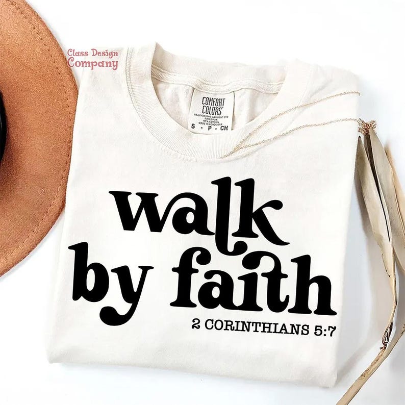May include: A white t-shirt with black text that reads "walk by faith 2 Corinthians 5:7".
