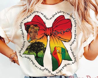 May include: A cream-colored t-shirt featuring a large red, yellow, and green bow graphic. The bow contains an illustration of a person, a tree, a raised fist, and a broken chain. The text "I am black history" circles the bow design.