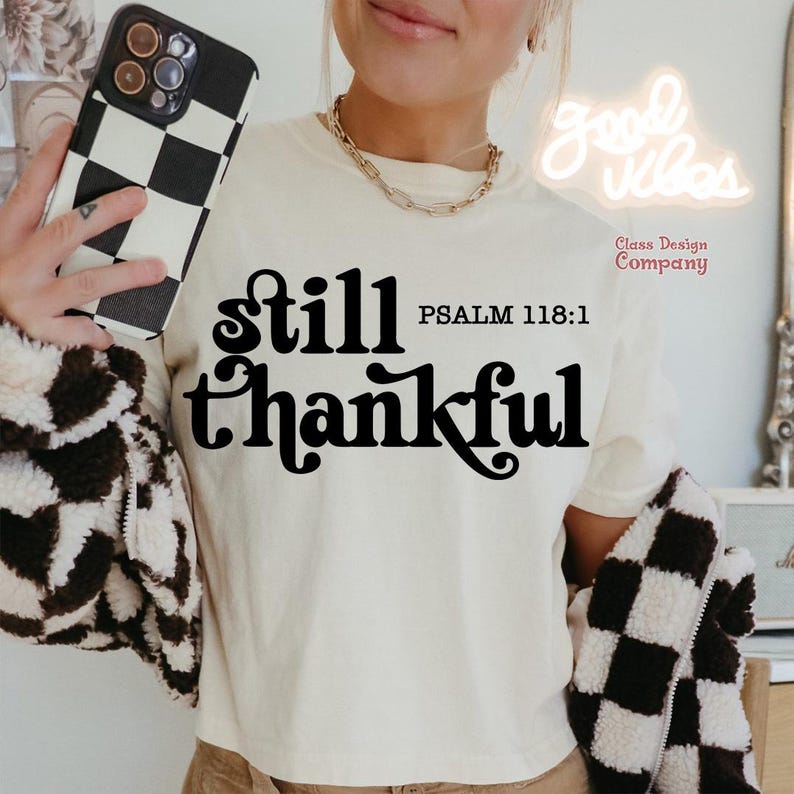 May include: A white t-shirt with the text "still thankful" in black, with the scripture reference "PSALM 118:1" below. The shirt is being worn by a person.