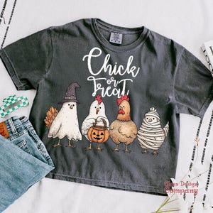 May include: Dark gray t-shirt with the words "Chick or Treat" in white script. The shirt features a graphic of four chickens dressed in Halloween costumes: a witch, a pumpkin carrier, a regular chicken, and a mummy.