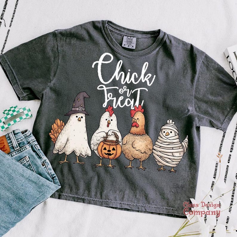 May include: Dark gray t-shirt with the words "Chick or Treat" in white script. The shirt features a graphic of four chickens dressed in Halloween costumes: a witch, a pumpkin carrier, a regular chicken, and a mummy.