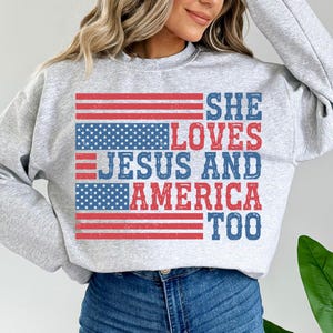 May include: Grey sweatshirt with a distressed American flag design and the text "She Loves Jesus and America Too".