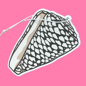 May include: A seashell-shaped air freshener with a white string for hanging. The design features a black and white pattern on the shell's exterior and a tan interior. The background is a solid pink.