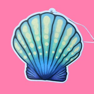 May include: A seashell-shaped air freshener with a gradient of blue hues, accented with light yellow spots and lines. The design features a white string for hanging, set against a vibrant pink background.