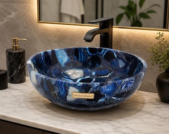 May include: A round vessel sink crafted from polished blue agate stone with deep navy and white crystalline patterns. The basin features a small rectangular gold-toned plaque with the text StoneCraftsInd centered on the front exterior surface.