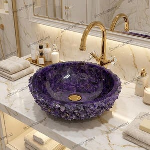May include: A luxurious purple stone bathroom sink with a gold faucet. The sink has a textured, crystal-like exterior and a smooth interior. The faucet has crystal handles. The sink is set on a white marble countertop.