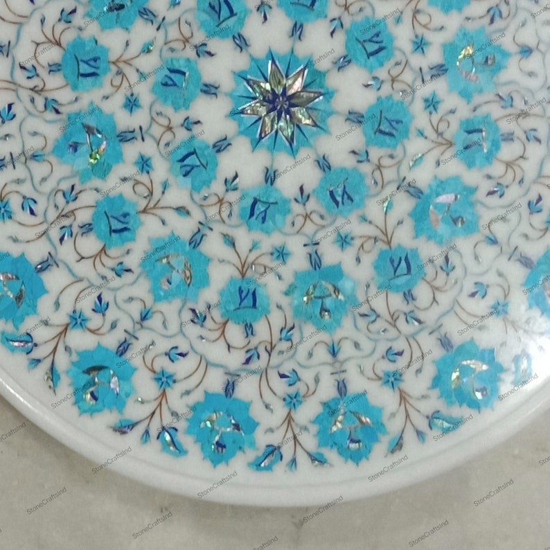 May include: A white marble table top with a floral design. The design features turquoise blue flowers and leaves with silver accents. The table has a white border and a polished finish. The overall theme is decorative and elegant.