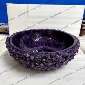 May include: A deep purple amethyst bowl with a rough, textured exterior and a smooth interior. The bowl is a rich shade of purple, showcasing the natural beauty of the gemstone. The bowl is a decorative item.