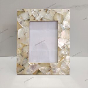 May include: A white picture frame with a decorative border made of iridescent mother of pearl shell pieces.