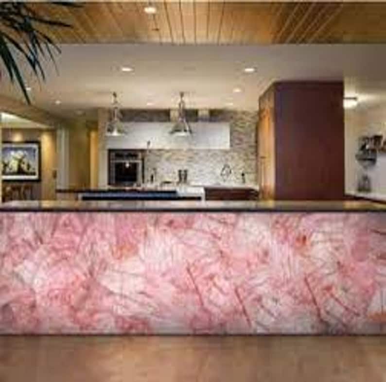 May include: A kitchen countertop with a pink and white marble-like surface. The countertop is made of a translucent material that allows light to shine through.