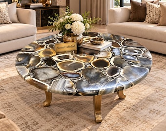 May include: A round coffee table featuring a polished surface made of inlaid black, gray, and white agate stone slices. The table is supported by three curved, metallic gold legs and includes a small rectangular sign labeled StoneCraftsInd.