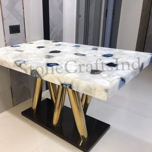 May include: A white agate dining table with blue and gray agate accents. The table has a gold metal base with four legs.