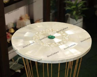 May include: A white round table top with a decorative inlay of mother of pearl and a green gemstone in the center. The table top is supported by a gold metal stand with vertical bars.