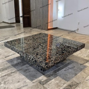May include: A square coffee table crafted from black agate with gold veins. The table features a polished, reflective surface and a distinctive, organic shape.