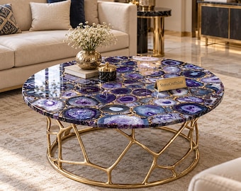 May include: A round coffee table featuring a polished surface made of purple agate slices with gold-toned edges. The base is constructed from a gold-colored metal frame with an organic, branch-like design. A small sign reads StoneCraftsInd.