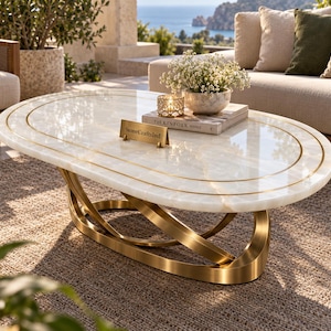 May include: An oval coffee table with a polished white stone top featuring gold-toned circular inlays. The base consists of interlocking curved gold metal bands. A small gold plaque on the surface displays the text StoneCraftsInd in black lettering.