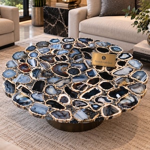 May include: A circular coffee table featuring a tabletop composed of numerous polished blue, black, and white agate slices arranged in a mosaic pattern. A small rectangular gold-toned plaque with the text StoneCraftsInd is attached to the surface.