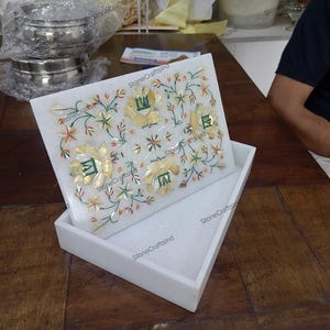 May include: A white marble box with a lid featuring a floral inlay design. The inlay includes yellow, green, and red accents. The box is rectangular and sits inside a matching white tray, showcasing a handcrafted decorative item.