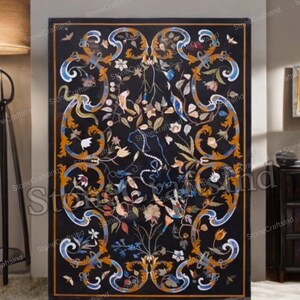 May include: A rectangular black marble table with an intricate floral inlay design. The design features colorful flowers, birds, and swirling patterns in shades of orange, blue, and white. The table has a dark border.
