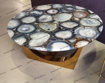 May include: A round coffee table with a unique agate stone top. The table has a gold metal base and features a variety of natural agate slices in shades of gray, brown, and white.