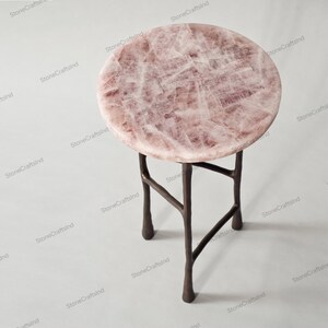 May include: A round pink quartz table top with a metal base. The base has four legs that are shaped like branches.