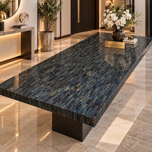 May include: A rectangular dining table featuring a polished surface made of small, vertically aligned blue and dark grey stone tiles. The table is supported by a solid, dark-colored pedestal base and displays a small gold plaque reading StoneCraftsInd.