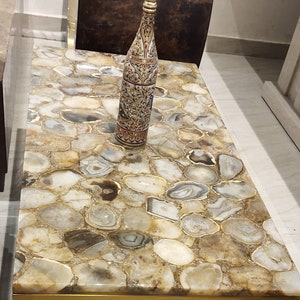 May include: A coffee table with a gold trim and a top made of agate stone. The table features a decorative bottle with intricate designs.