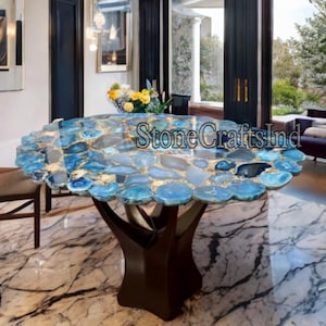 Pode incluir: Uma mesa de jantar redonda com um tampo único de pedra de ágata azul e uma base de madeira castanho escura. A mesa está num ambiente doméstico moderno.