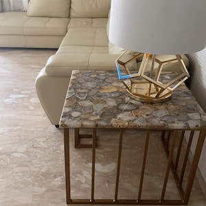 May include: A gold metal side table with a geometric base and a top made of agate stone. The table has a white lamp with a geometric shade on top.