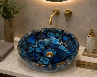 May include: A round vessel sink crafted from polished blue agate stone slices with gold-toned accents and a central gold drain. The basin features a mosaic of deep blue and translucent stone segments, creating a vibrant, multi-tonal surface.