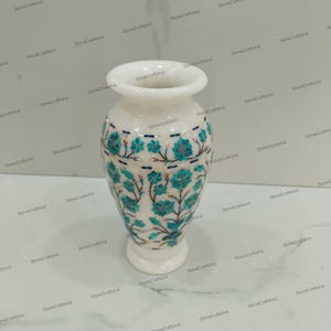 May include: White marble vase featuring a floral design in turquoise and red. The vase is decorated with intricate details and is a fine example of traditional craftsmanship.