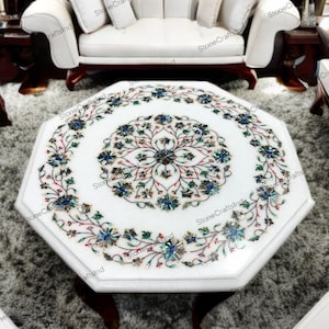 Puede incluir: Mesa de centro octogonal de mármol blanco con intrincado diseño floral incrustado en tonos azules, verdes y rojos. La mesa tiene patas de madera oscura y está en un salón.