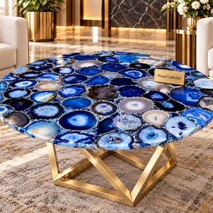 May include: A round coffee table featuring a tabletop composed of numerous blue and white agate slices with a polished finish. The table is supported by a geometric gold-toned metal base. A small rectangular plaque reads StoneCraftsInd.