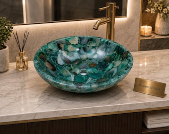 May include: A round vessel sink crafted from polished green agate stone slices, featuring a mosaic pattern of translucent teal, emerald, and dark green mineral segments with a smooth, glossy finish and a central drain hole, next to a gold nameplate.
