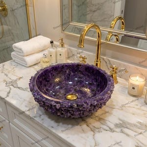 May include: A luxurious purple amethyst stone sink with a textured, crystalline exterior. The sink is set on a marble countertop with a gold faucet and fixtures. A candle and toiletries are also visible.