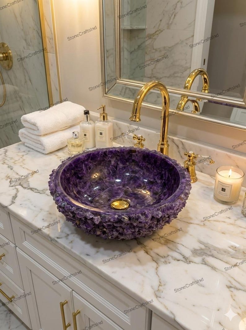 May include: A luxurious purple amethyst stone sink with a textured, crystalline exterior. The sink is set on a marble countertop with a gold faucet and fixtures. A candle and toiletries are also visible.