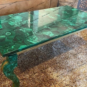Op de afbeelding: Een groene malachiet salontafel met goud geverfde poten. Het tafelblad heeft een draaiend patroon van groen en zwart.