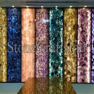May include: A display of agate slabs in various colours, including blue, purple, green, and brown. The slabs are backlit, highlighting the intricate patterns and textures of the stone. The text "Stone Crafts India" is visible in the centre of the image.