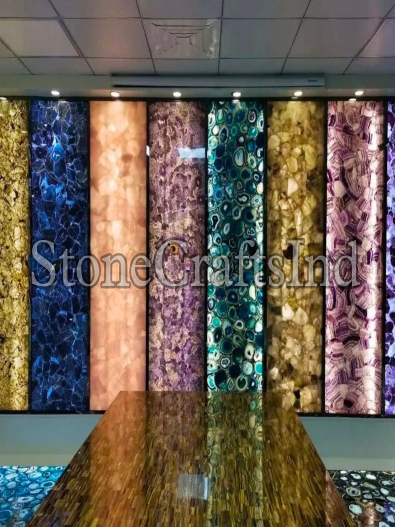 May include: A display of agate slabs in various colours, including blue, purple, green, and brown. The slabs are backlit, highlighting the intricate patterns and textures of the stone. The text "Stone Crafts India" is visible in the centre of the image.