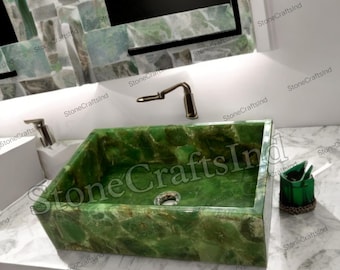 May include: A rectangular, green stone bathroom sink with a polished finish. The sink is set on a white countertop, with a matching green stone backsplash and a bronze faucet. The sink is a unique, decorative element for a bathroom.