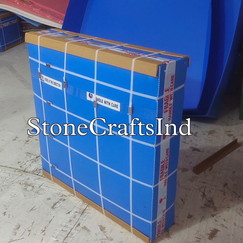 May include: A blue cardboard box with a brown top is wrapped in white tape and labelled "FRAGILE HANDLE WITH CARE". The box is sitting on a concrete floor. The text "StoneCraftsInd" is visible on the box.