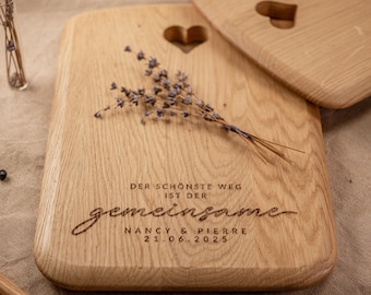 May include: Two wooden cutting boards with a heart-shaped cutout and engraved text. One board has a sprig of lavender. The text reads "DER SCHÖNSTE WEG IST DER gemeinsame NANCY & PIERRE 21.06.2025".