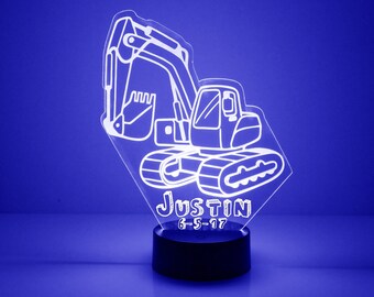 May include: White outline of an excavator with the name Justin and the date 6-5-17 on a clear acrylic night light with a black base.