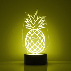 May include: A white pineapple-shaped night light with the name "Mia" inscribed on the fruit. The light is on and illuminating the pineapple.