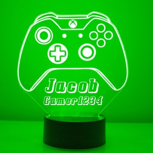 May include: A green illuminated gaming controller-shaped night light. The controller design features buttons and a directional pad. The name "Jacob" and "Gamer1234" are displayed below the controller. The base is black.