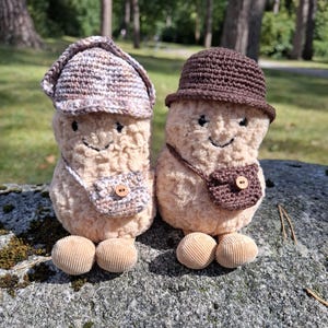 Puede incluir: Dos figuras de champi&ntilde;ones de peluche con caras sonrientes, que llevan sombreros y bolsos peque&ntilde;os de ganchillo. Los champi&ntilde;ones tienen pies de pana y est&aacute;n sobre un fondo natural. Los sombreros y los bolsos son en tonos marrones y beige.