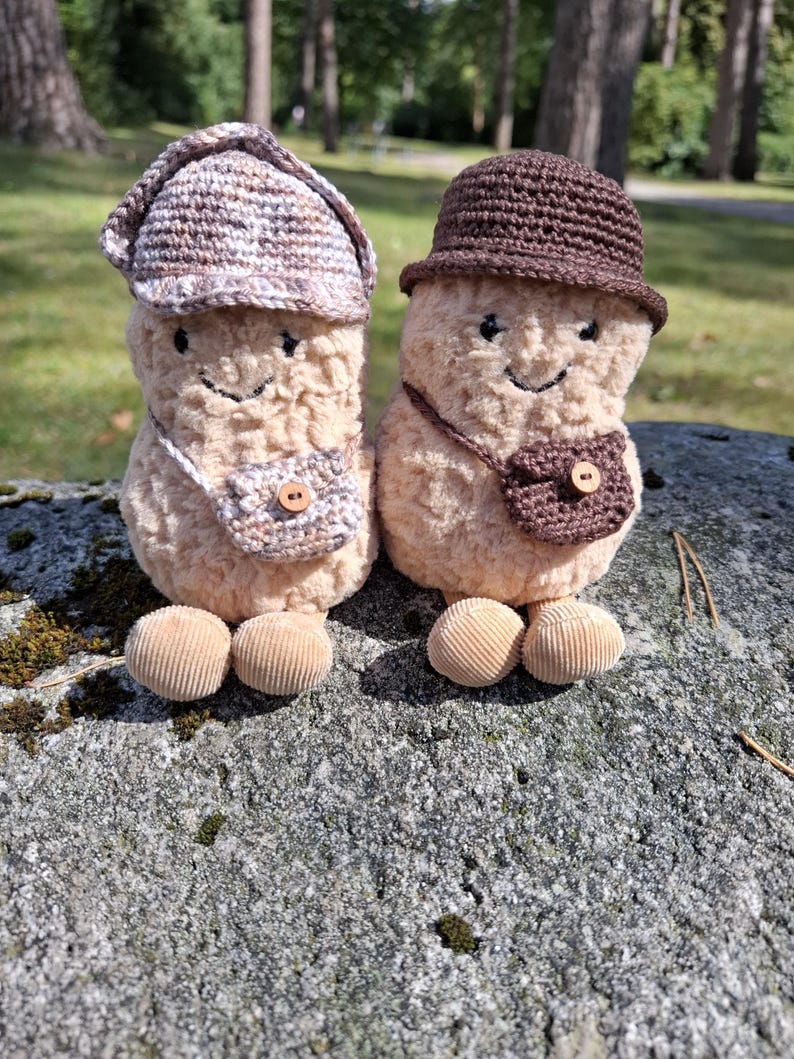 Puede incluir: Dos figuras de champi&ntilde;ones de peluche con caras sonrientes, que llevan sombreros y bolsos peque&ntilde;os de ganchillo. Los champi&ntilde;ones tienen pies de pana y est&aacute;n sobre un fondo natural. Los sombreros y los bolsos son en tonos marrones y beige.